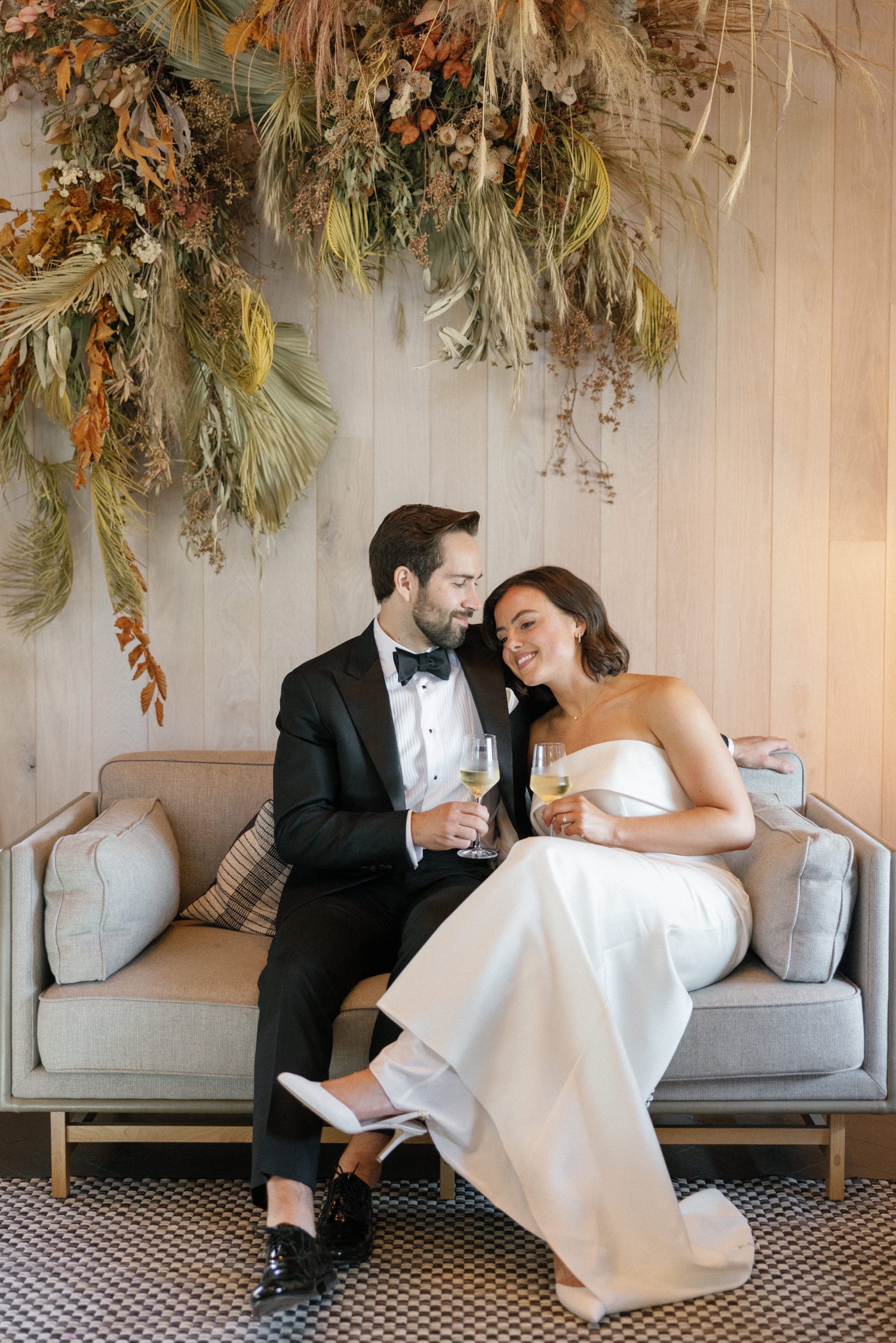 https://fetch.getnarrativeapp.com/static/1f660019-b49f-4837-a24a-1cae9e0f314c/smiling-bride-in-white-dress-sitting-on-loveseat-with-groom-in-black-tuxedo-on-stanly-ranch-wedding-day.jpg?w=1500