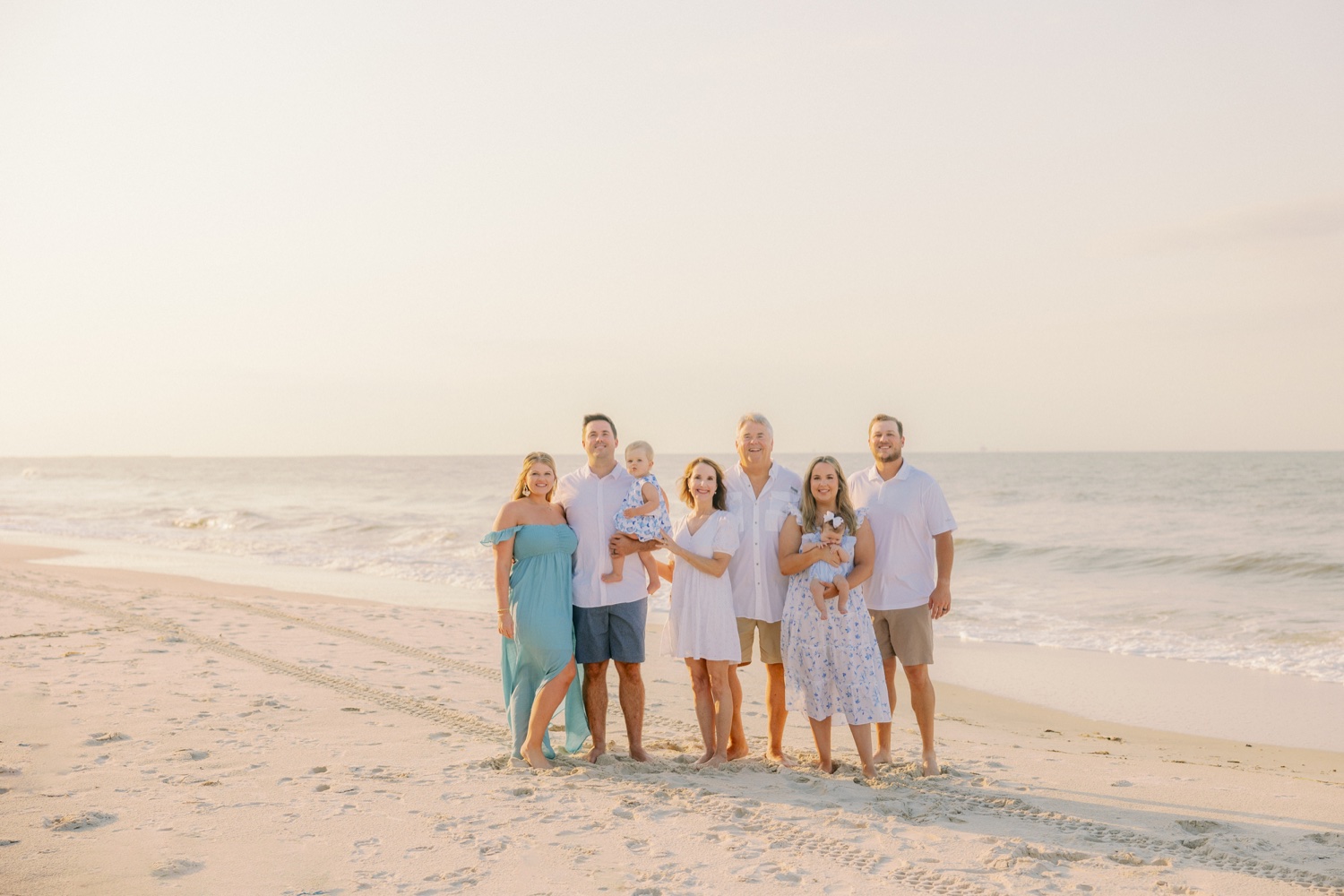 An endearing snapshot of the Yancey family, gathered on Dauphin Island. The morning sunlight bathes them as they huddle together sharing smiles, showcasing the genuine warmth and deep bond they share. The serene backdrop of the island enhances the beauty of the moment.