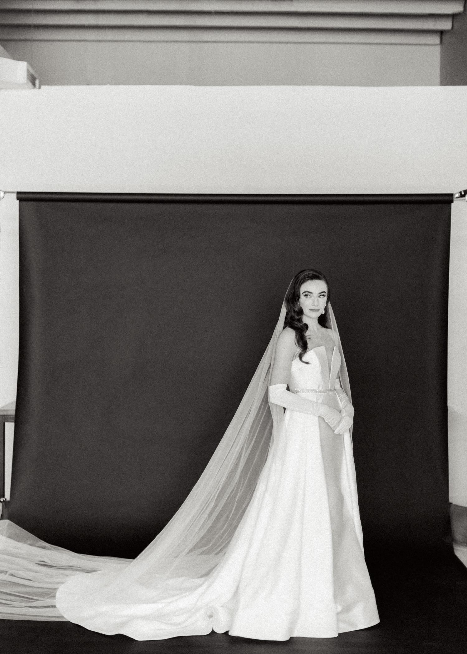 https://fetch.getnarrativeapp.com/static/b55a5091-1c14-4f36-8bad-89dbb4762631/Bride-in-white-Galia-Lahav-wedding-dress,-overskirt,-gloves,-and-veil-during-studio-bridal-session-with-black-backdrop.jpg?w=1500