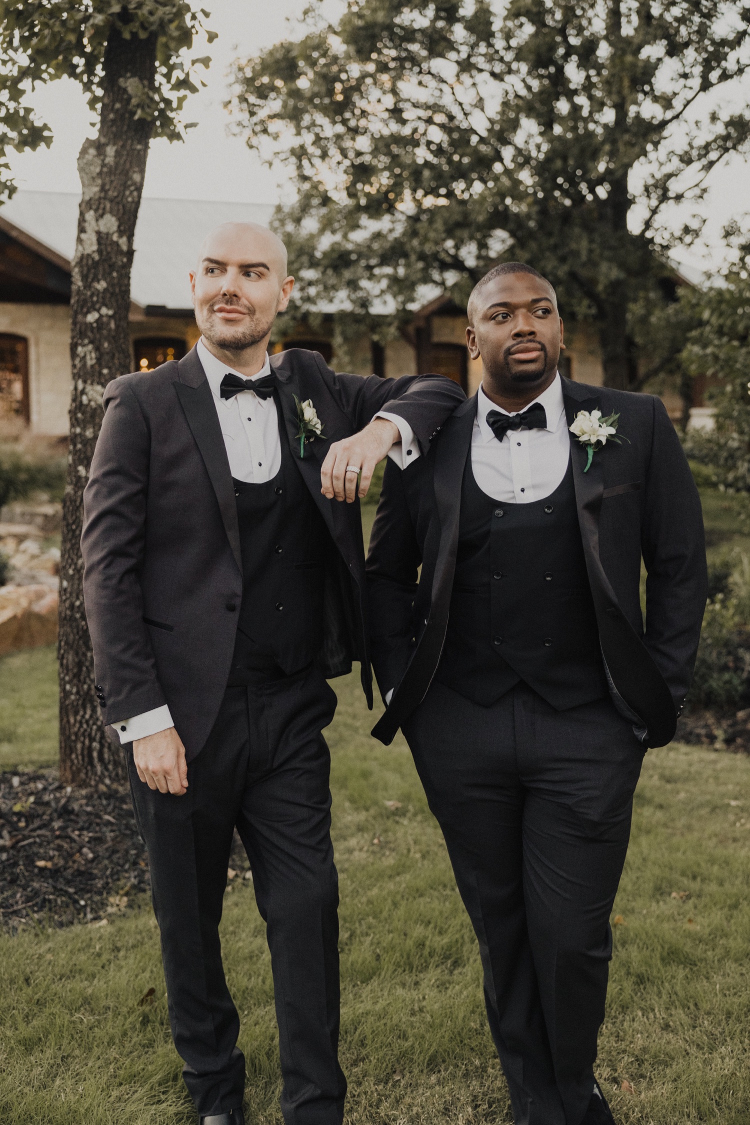 Two grooms in tuxedos posing at a wedding venue.